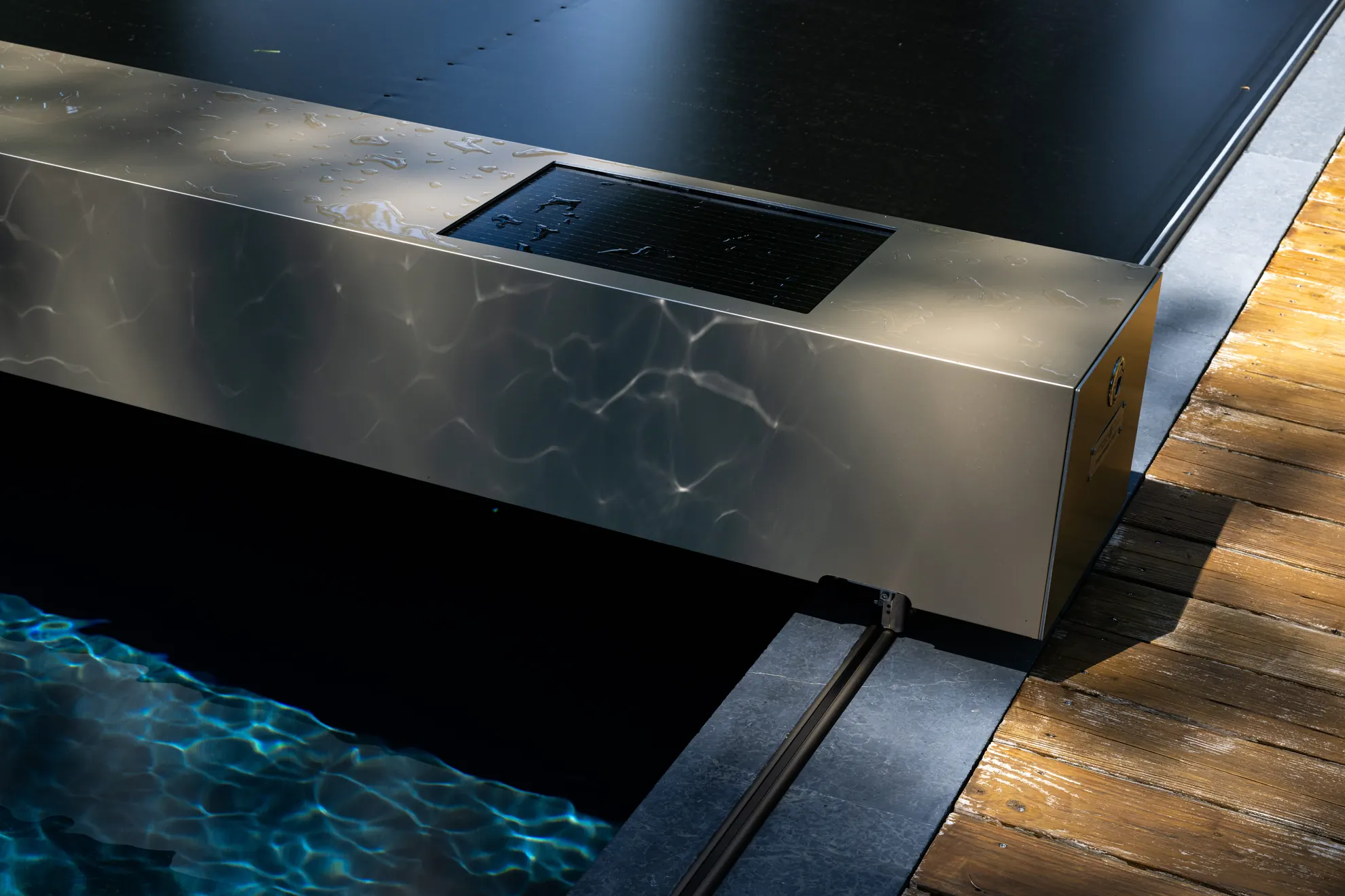 Gros plan sur l'habillage effet bronze d’une couverture de piscine Coverseal, avec membrane noire et terrasse en bois